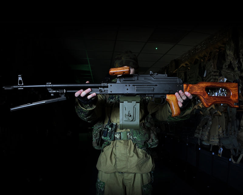 Person in military gear holding an A&K PKM Airsoft Support Gun in a dark setting